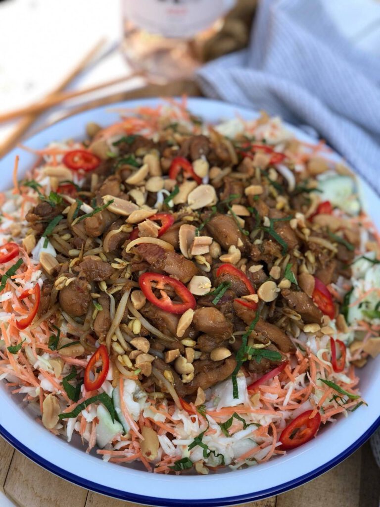 salade met kip ketjap en knapperige pinda's geserveerd in witte schaal