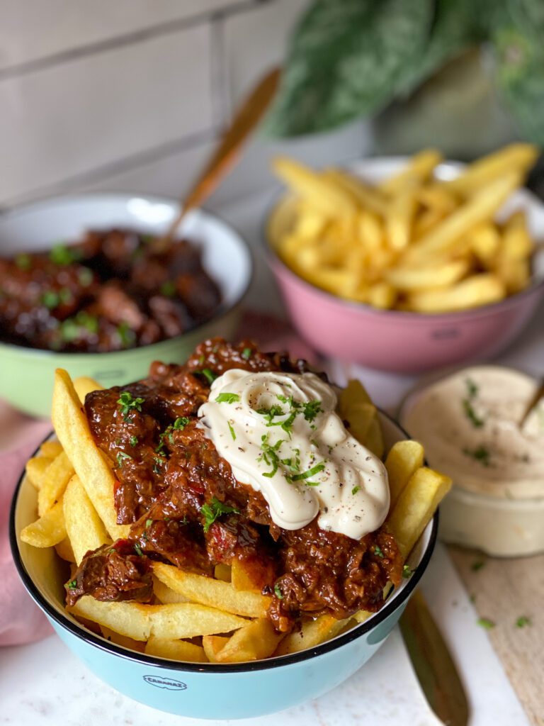 een schaaltjes gevuld met frietjes, stoofvlees en geserveerd met mayonaise 