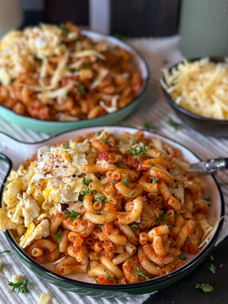 macaroni met verse worst in tomatensaus geserveerd op een rond bord met roerei en geraspte kaas