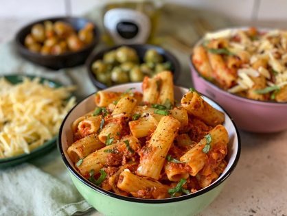 penne met tonijn in tomatensaus in een schaaltje en erbij geserveerd met geraspte kaas en olijven