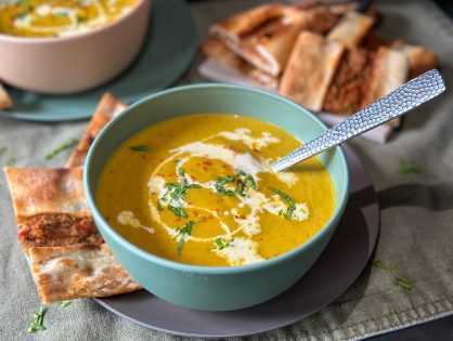 romige wortelsoep met courgette, geserveerd in een rond schaaltje met een drizzle room.