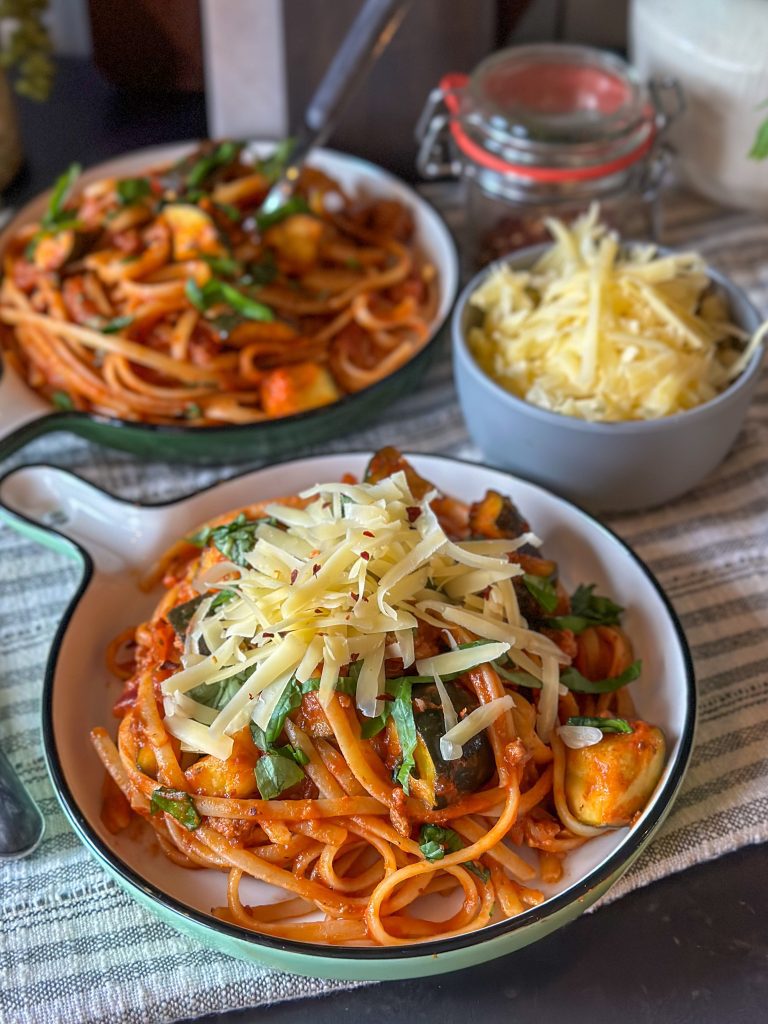 pasta in tomatensaus met gehakt en courgette, geserveerd met geraspte kaas en verse basilicum op een rond bord