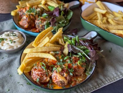 gehaktballetjes uit de oven met sweet chilisaus geserveerd met frietjes en mayonaise op een rond bord.