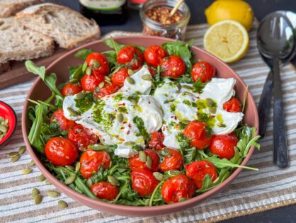 een schaal met salade Caprese met geroosterde tomaten, burrata, geserveerd met basilicum olie en pompoenpitten