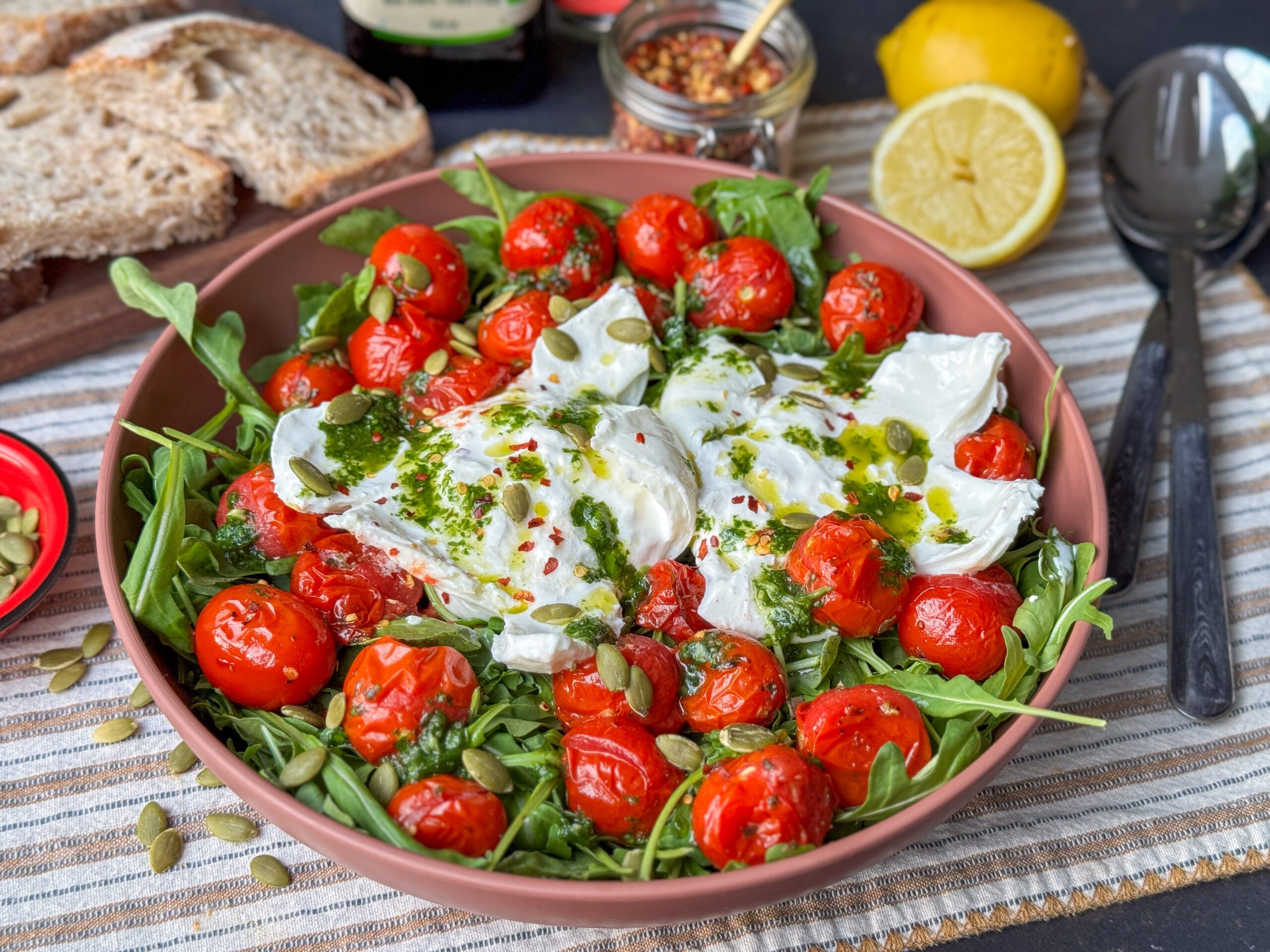 een schaal met salade Caprese met geroosterde tomaten, burrata, geserveerd met basilicum olie en pompoenpitten