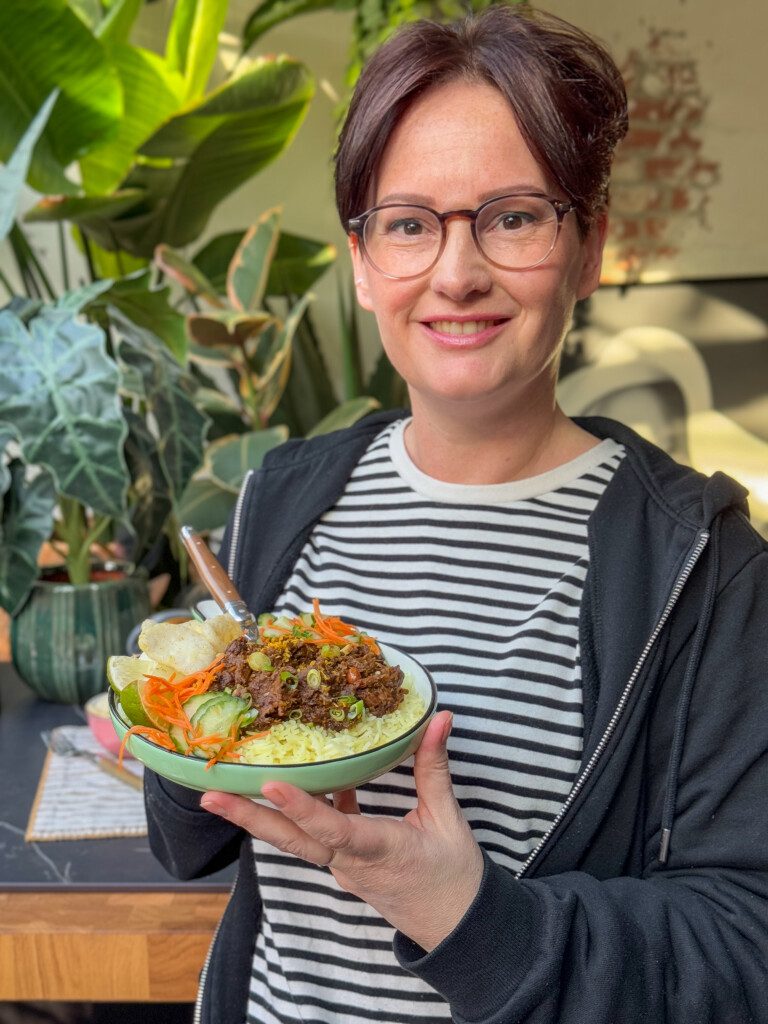 Marie Louise houdt rond bord vast met rendang stoofvlees geserveerd met komkommer en wortel in zuur. 