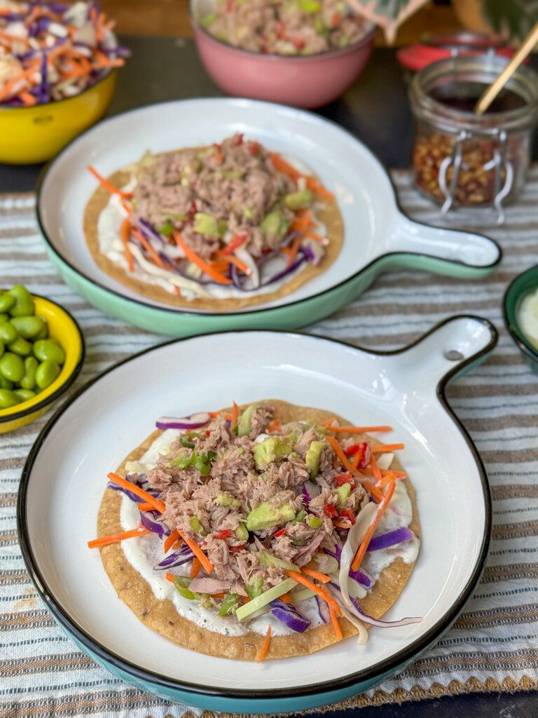 krokante tostada met tonijnsalade met avocado, koolmix en sojaboontjes op een rond klein bord.