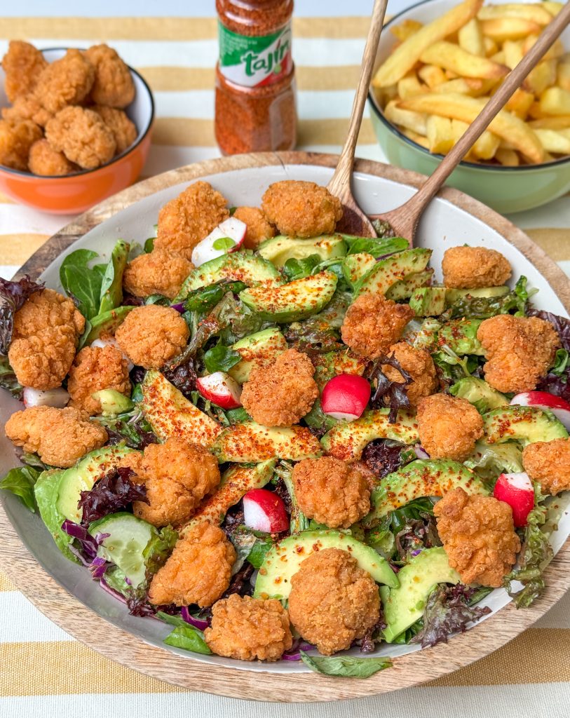 salade met kipnuggets geserveerd in een schaal met frietjes en losse stukjes kip op de achtergond