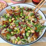 gyoza salade met edamame en pittige dressing geserveerd in witte schaal met pinda's en crispy chili olie