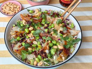 gyoza salade met edamame en pittige dressing geserveerd in witte schaal met pinda's en crispy chili olie