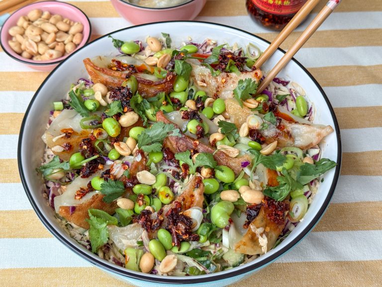 gyoza salade met edamame en pittige dressing geserveerd in witte schaal met pinda's en crispy chili olie