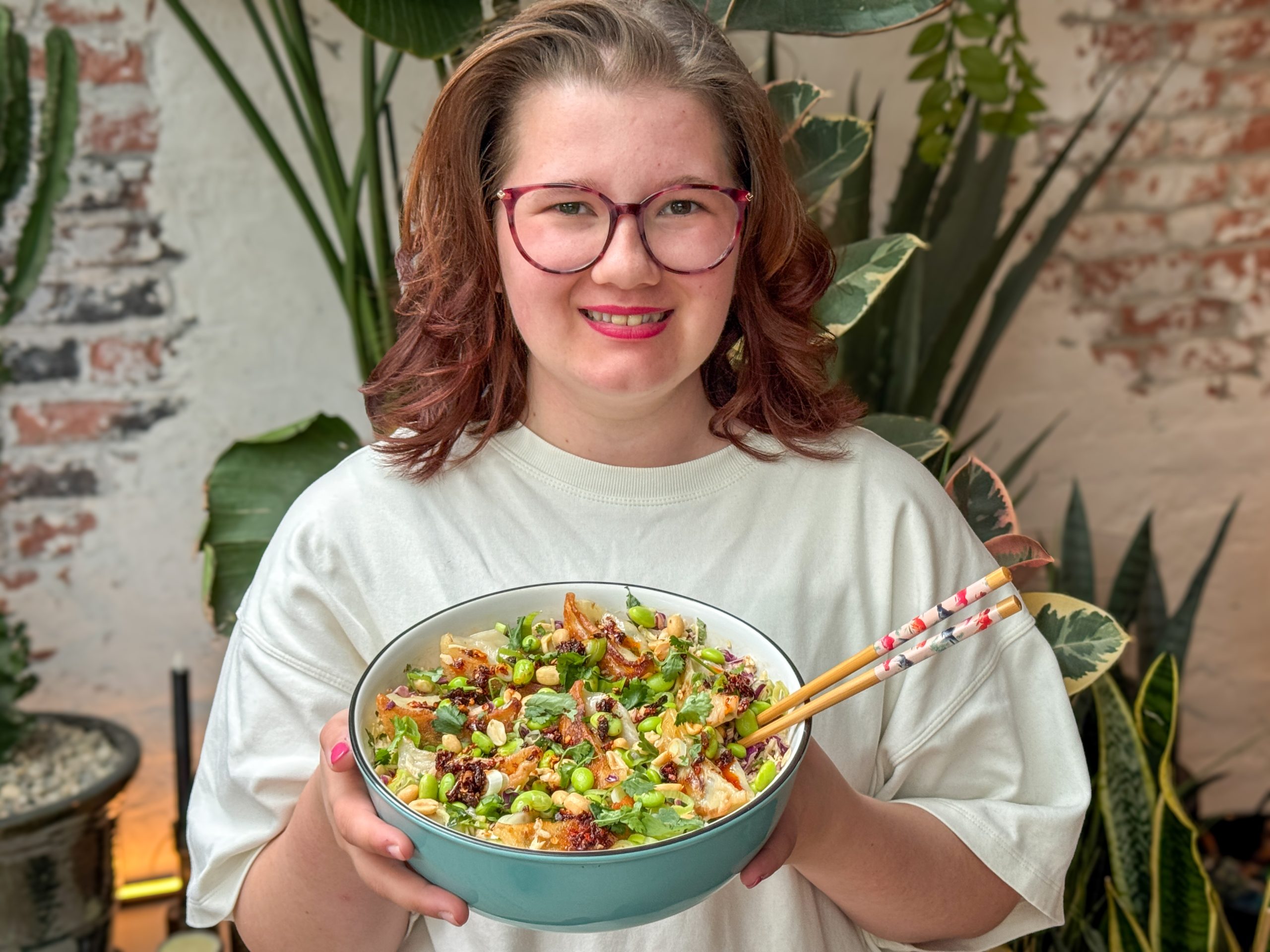 gyoza salade met crispy chili olie - vrouw houdt schaal met gyoza salade, edamame en pinda's vast