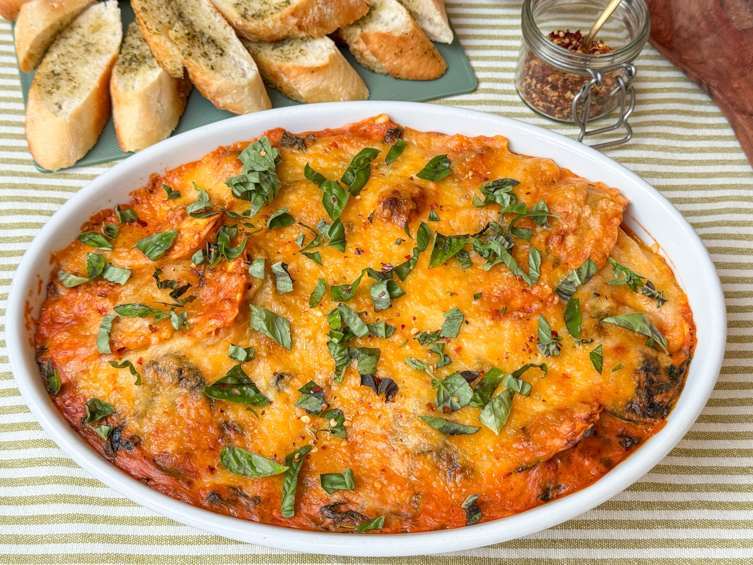 ravioli ovenschotel met spinazie in romige tomatensaus, in witte ovenschaal met gesmolten kaas