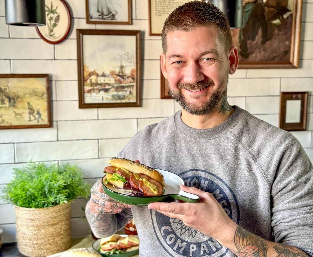 Broodje warme grillworst met pittige kerriemayonaise op bord vastgehouden door Jan Willem