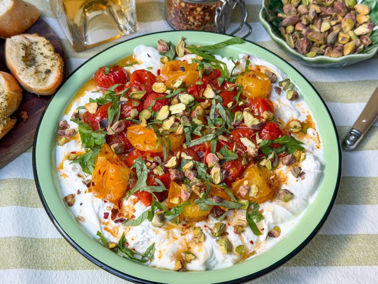 burrata dip met geroosterde tomaten, basilicum en pistachenoten op groen bord