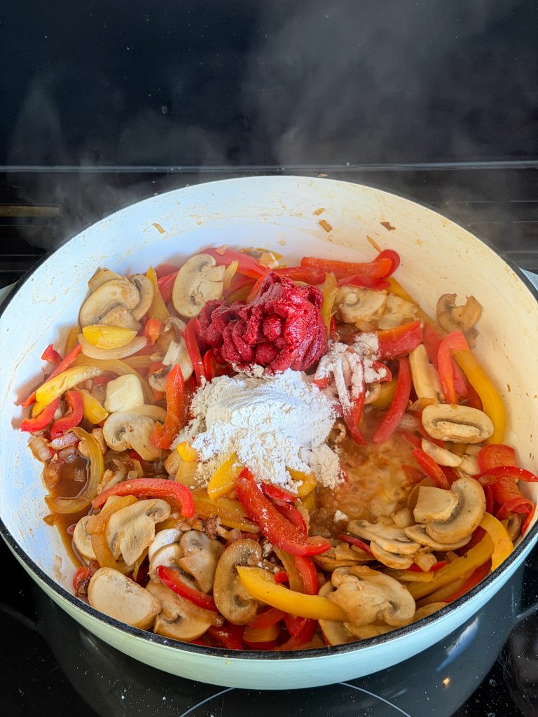 paprika en champignons met tomatenpuree en bloem in de pan, klaar voor de stroganoff saus