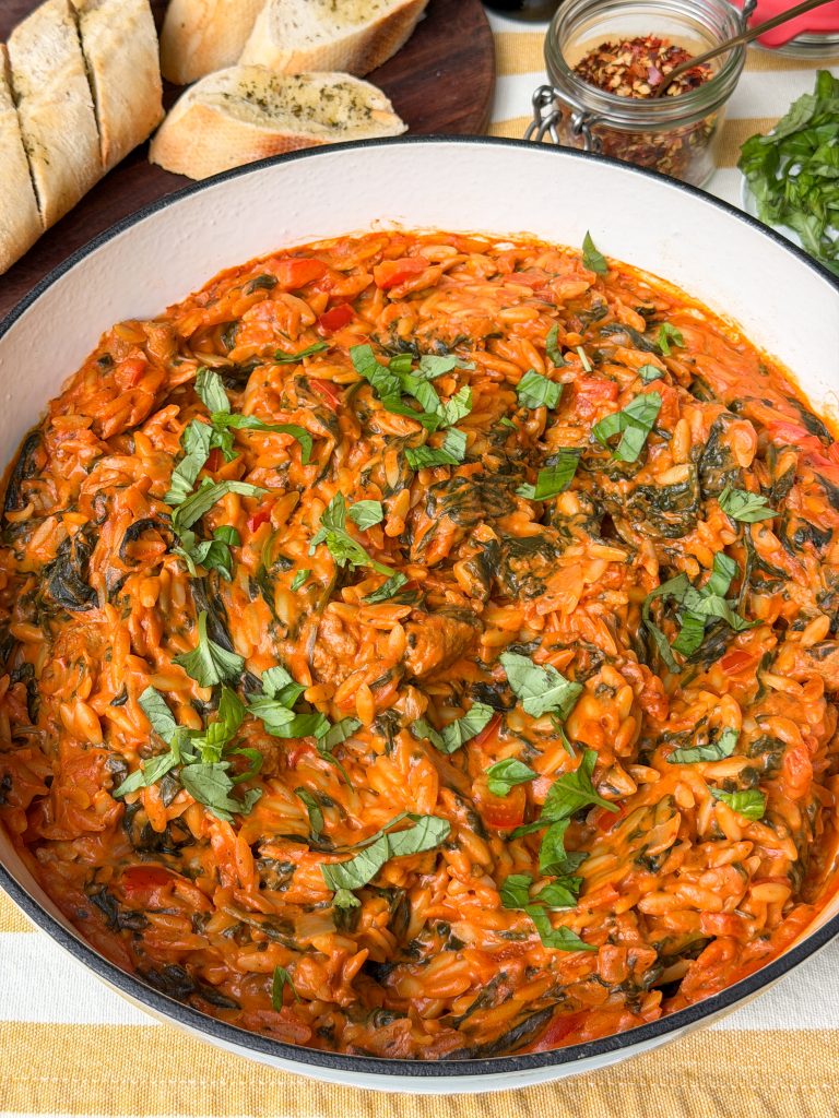 Eenpansgerecht orzo in romige tomatensaus met verse basilicum en kruidenstokbrood op tafel