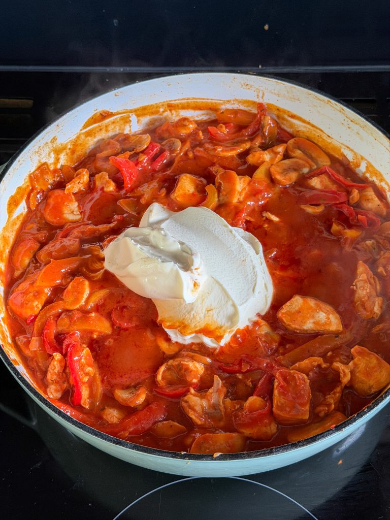 romige saus met crème fraîche toegevoegd aan de paprika en kip in de pan