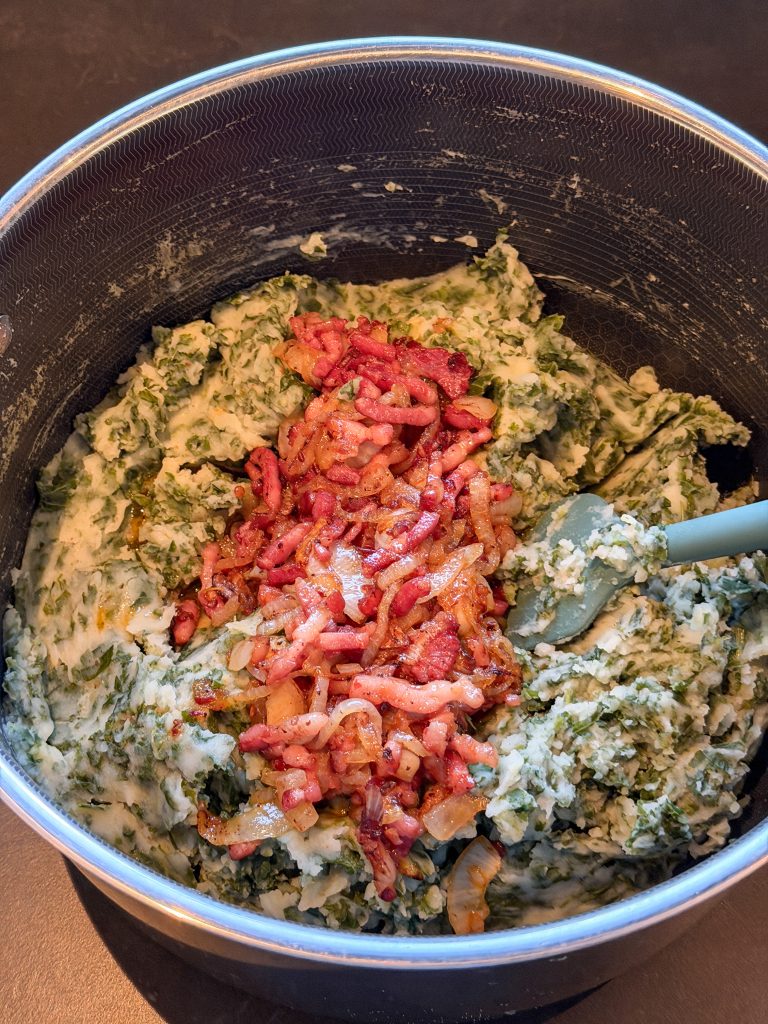 gebakken spekjes en uien worden door de romige boerenkoolstamppot geroerd.