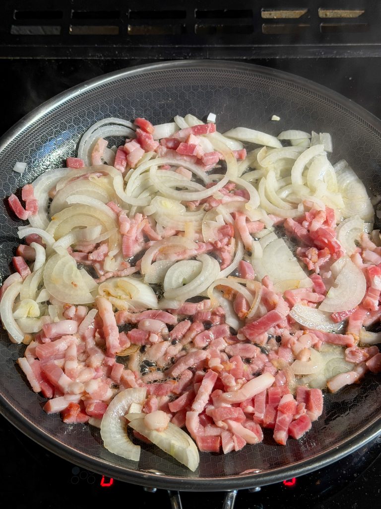 uien en spekjes worden gebakken in koekenpan voor extra smaak bij de boerenkoolstamppot