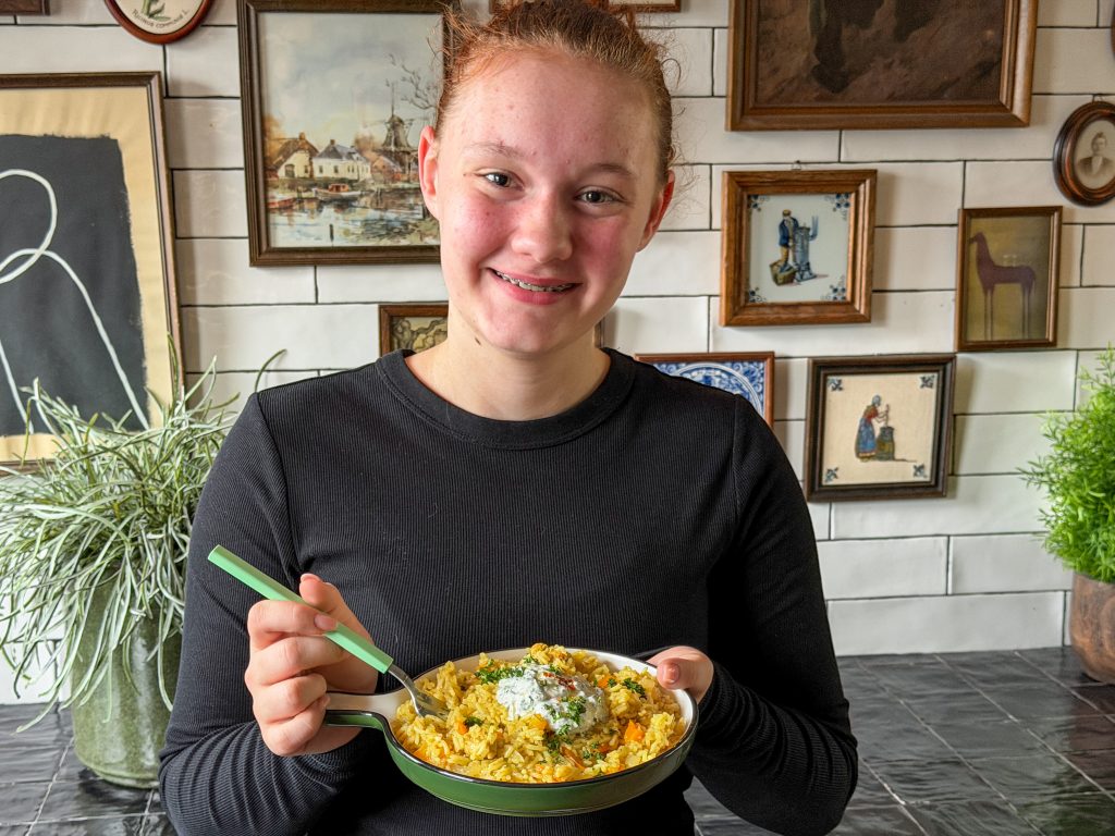 Amaranthe die een bord eenpansgerecht met rijst en kip vasthoudt en glimlacht