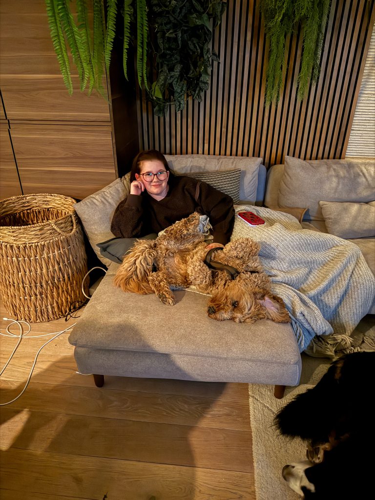 Beaudine chillend op de bank met de hond die languit naast haar ligt na een drukke dag.