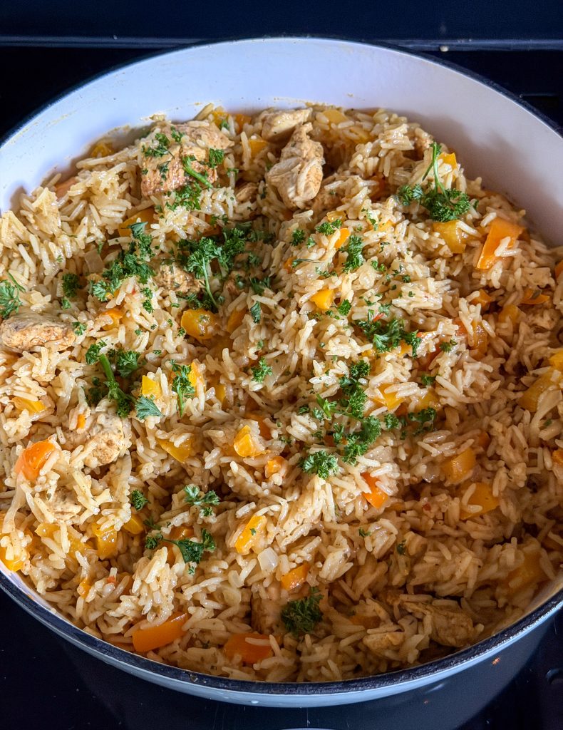 Eenpansgerecht met rijst en kip in vadouvan, bestrooid met verse peterselie