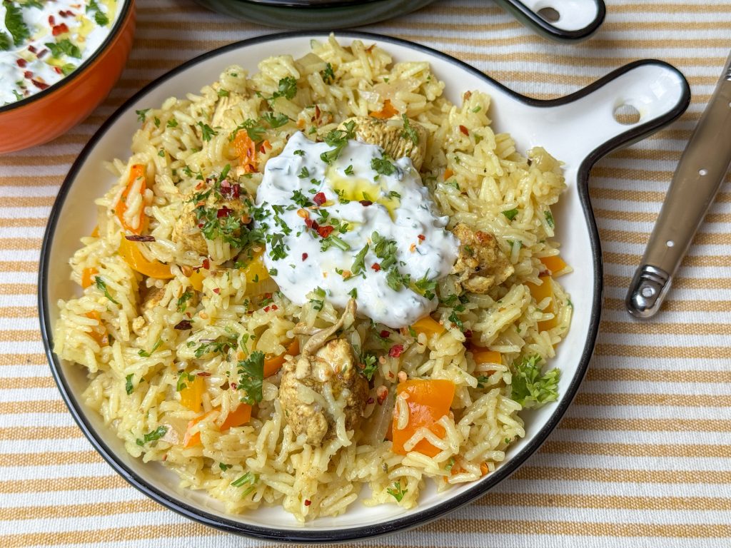 Bord met eenpansgerecht van rijst en kip met frisse yoghurtdip en kruiden