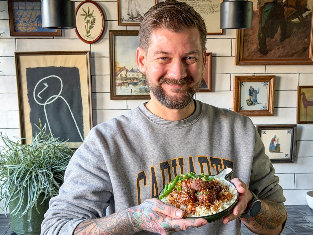 Man houdt bord met gehaktballetjes in zoetzure saus en rijst vast en glimlacht