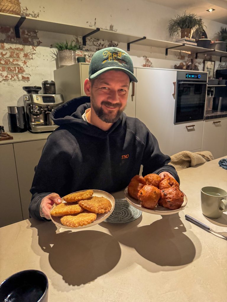 Jan Willem houdt twee borden met krokante appel beignets en oliebollen vast aan de keukentafel.