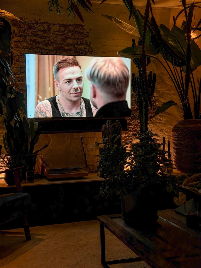 Televisie speelt een programma af in een donkere, sfeervol verlichte woonkamer met veel planten.