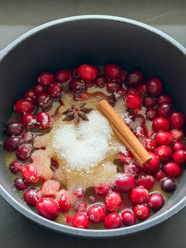 Cranberries in een pan met sinaasappelsap, suiker, kaneelstokje en steranijs
