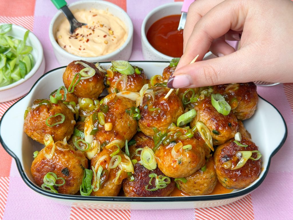 Hand pakt een kipgehaktballetje met cheddar en bosui uit een schaaltje