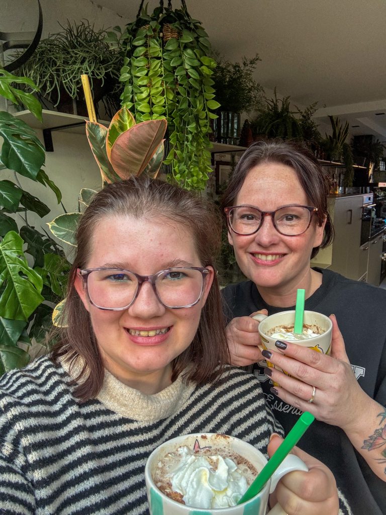 Thuis bij familie over de kook: week 49. Beaudine en Marie-Louise lachen terwijl ze samen warme chocolademelk drinken.