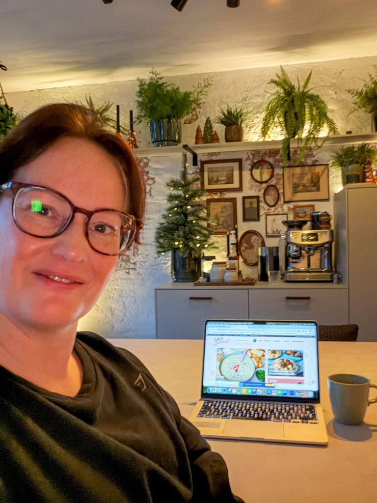 Marie-Louise werkt aan de keukentafel met haar laptop, omringd door gezellige kerstdecoratie.