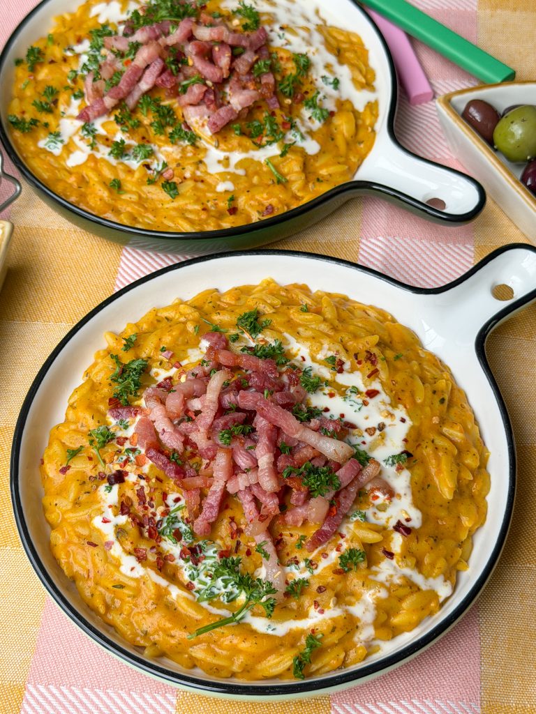 Orzo eenpansmaaltijd in romige pompoensaus geserveerd met krokante spekjes