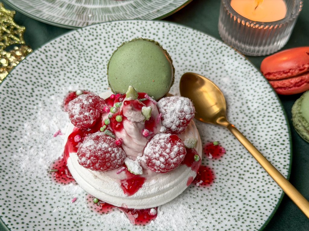 Pavlova met frambozen op groen bordje met groene macaron, geserveerd als kersttoetje