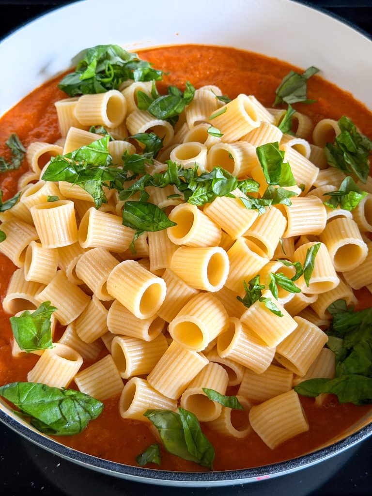 Gekookte pasta en verse basilicum toevoegen aan de saus