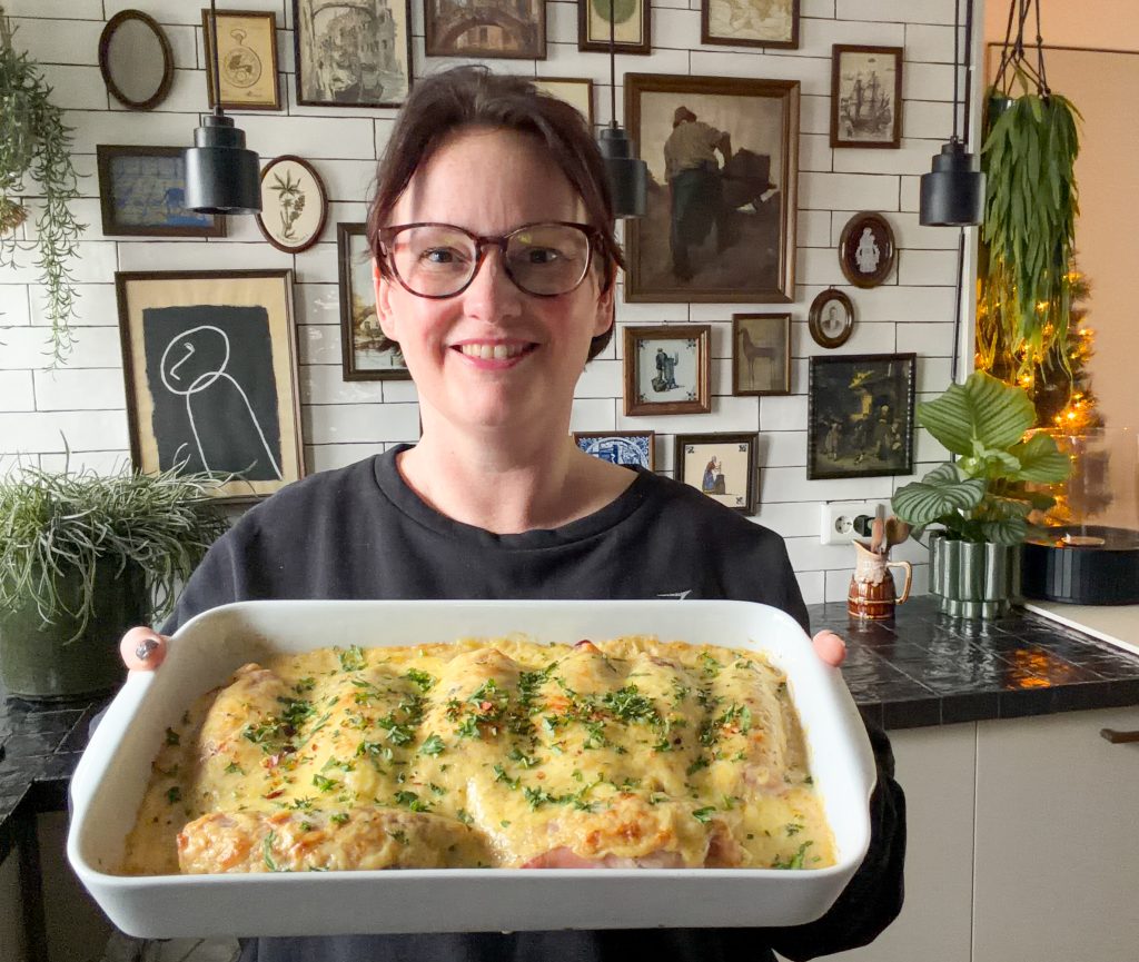 Marie Louise houdt schaal witlof met ham en kaas uit de oven vast, recept uit weekmenu 51
