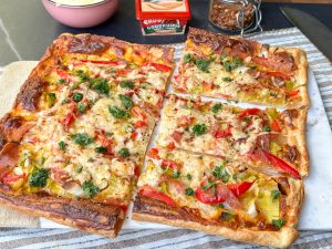 Plaattaart met pittige smeerkaas, paprika, prei en salami in stukken gesneden