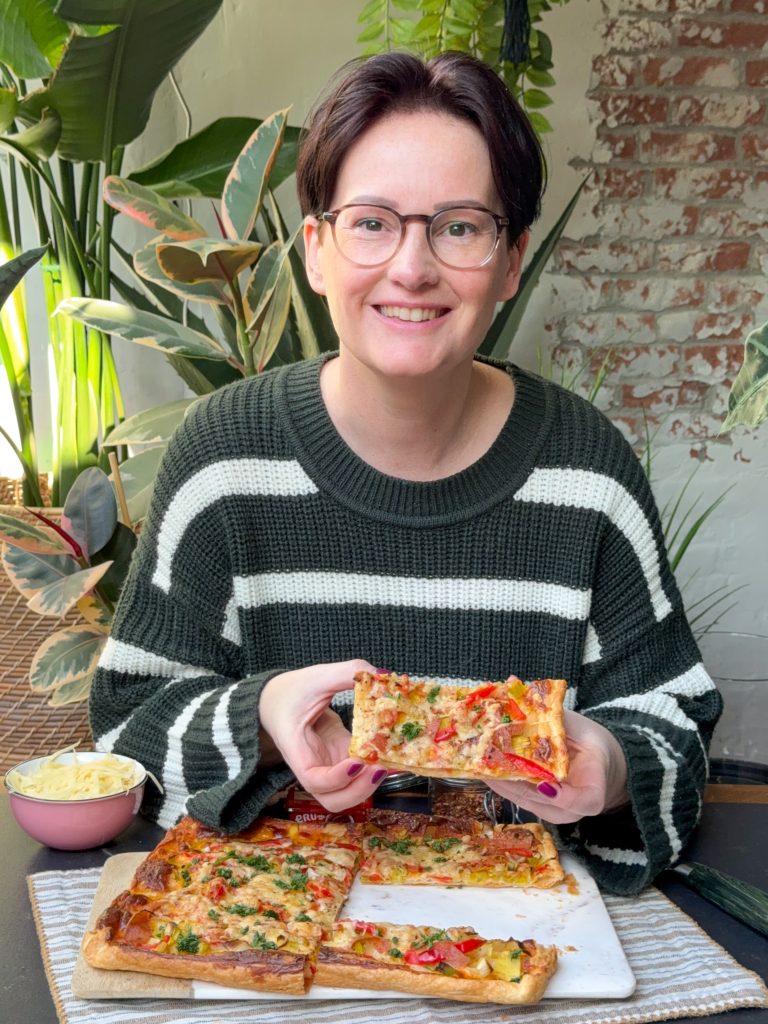 Stuk plaattaart met pittige smeerkaas, paprika, prei en salami vastgehouden aan tafel