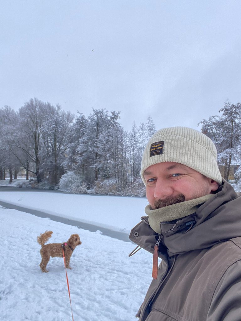 Winterse wandeling met hond langs het water in een besneeuwd landschap.